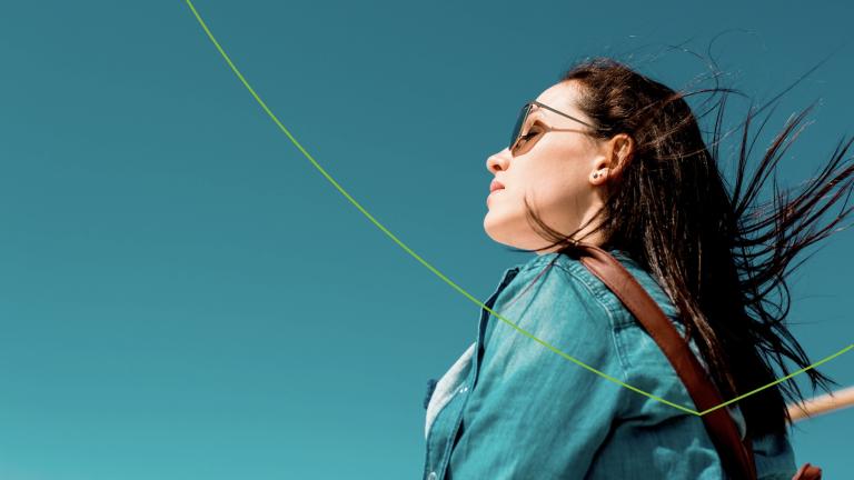 Vrouw met zonnebril staat in de zon met een blauwe lucht op de achtergrond