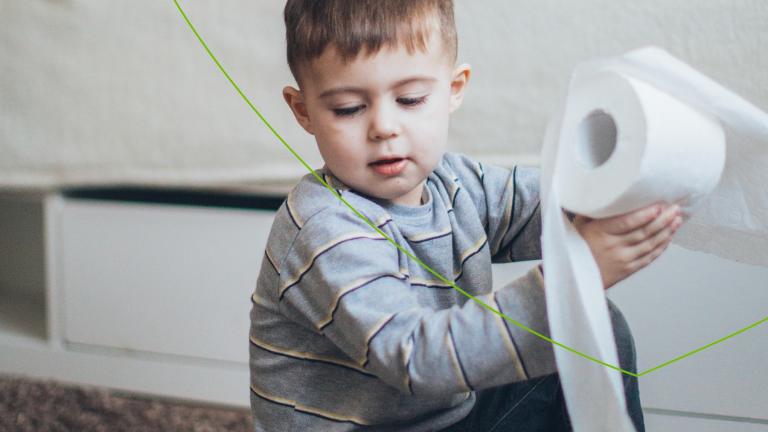 jongetje met streepjesshirt zit met wc-rol in zijn hand op de grond